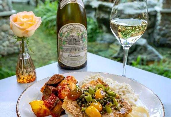 Plated fish entrée with vegetables and Far Niente Chardonnay at Heron restaurant’s garden‑inspired dining area at Little River Casino Resort in Manistee, Michigan.