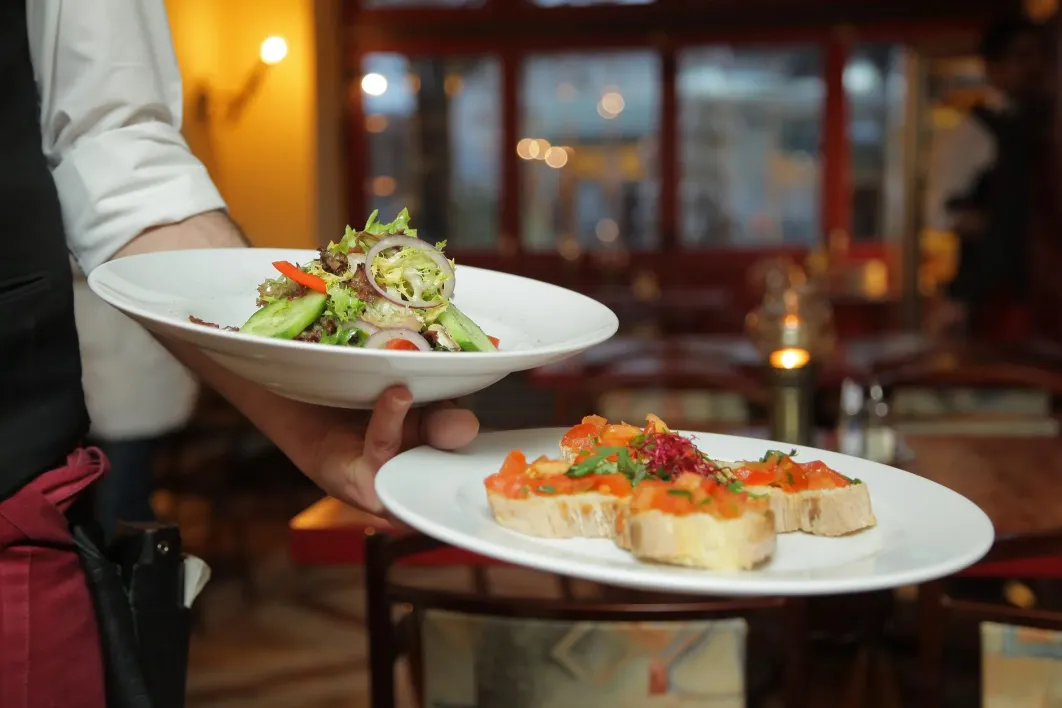 Restaurant waiter holding two plated dinners on one arm