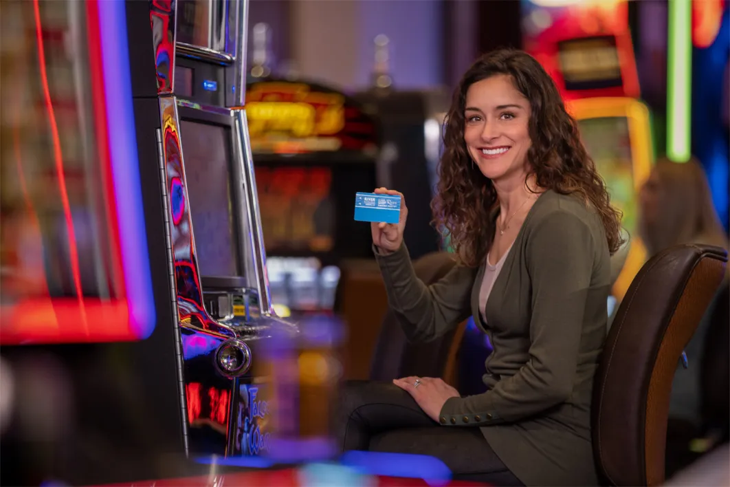 Brunette woman sitting at a slot machine holding a little river player's club card